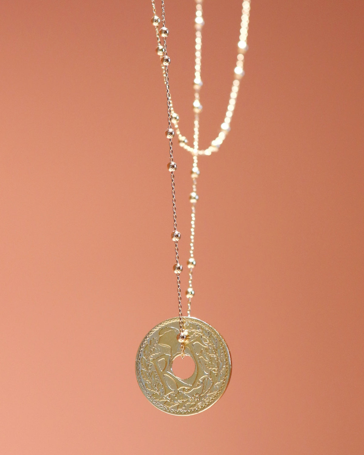 Collier Le Grand Nantais plaqué or : chaîne et pendentif pièce de monnaie sur fond terracotta